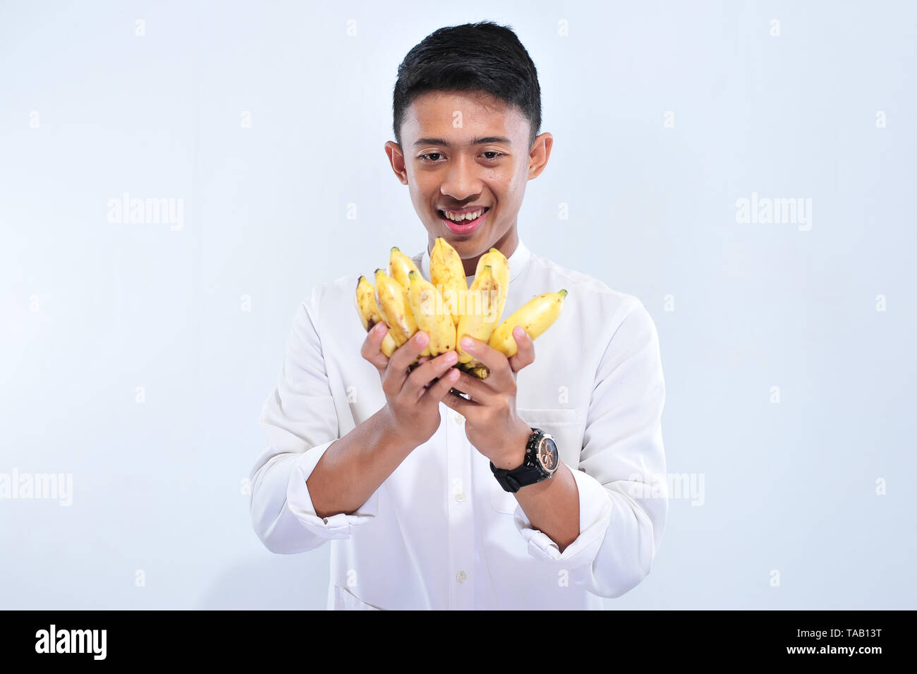 Young muslim man happy fasting when breaking the fast (Iftar) and suhoor eat yellow banana islolated in white background Stock Photo