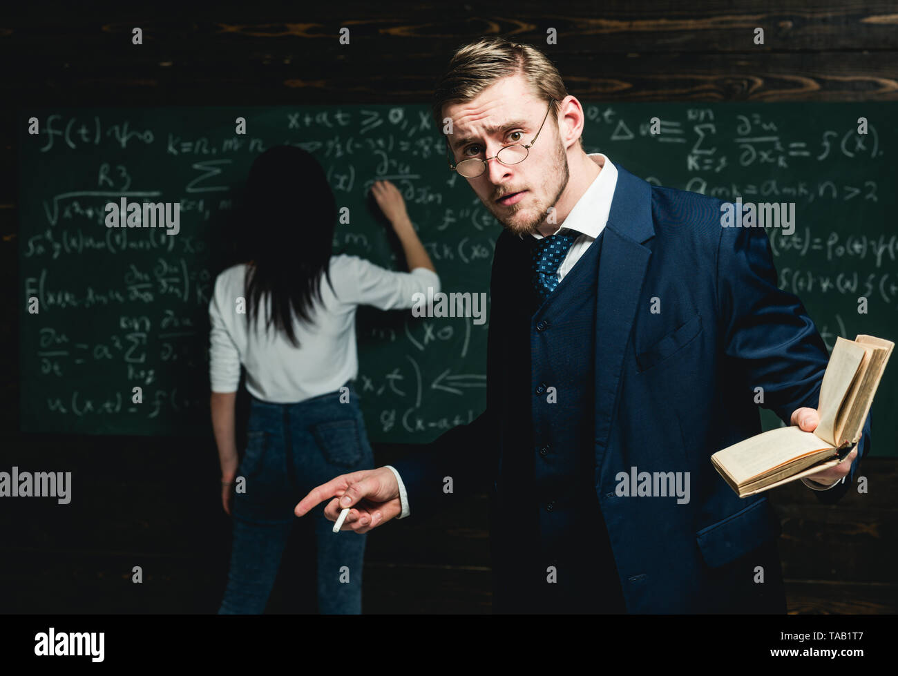 Teacher holding a book in front of a chalkboard looking surprised Stock ...