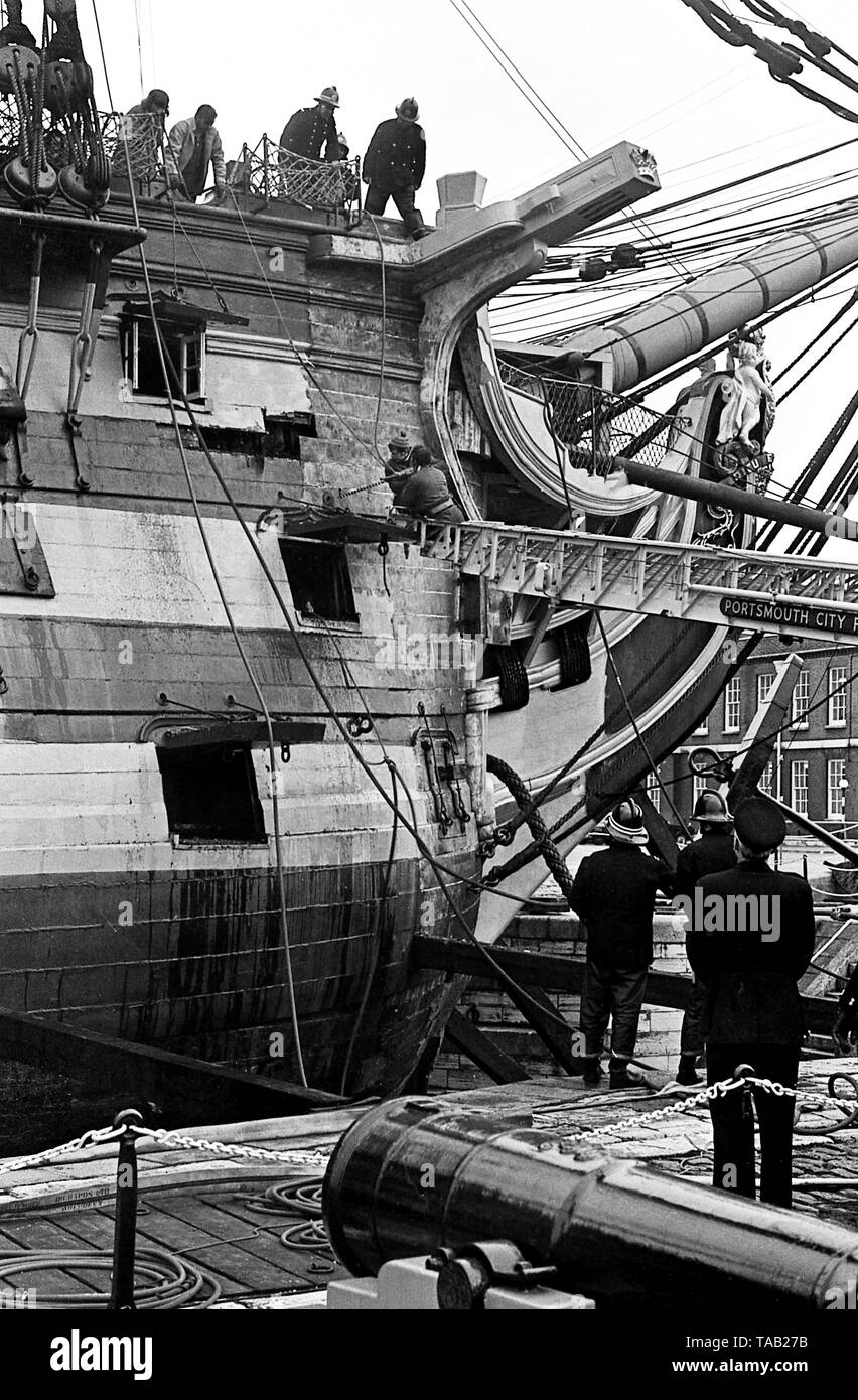 AJAXNETPHOTO. 27TH FEBRUARY, 1973. PORTSMOUTH,ENGLAND - FIRE IN THE HOLE! - MEMBERS OF PORTSMOUTH CITY FIRE BRIGADE STRUGGLE TO PUT OUT A FIRE IN ADMIRAL HORATIO NELSON'S FAMOUS TRAFALGAR FLAGSHIP H.M.S. VICTORY, STARTED WHILE RESTORERS WERE REMOVING OLD PAINT FROM INSIDE THE BOW SECTION. FIREMEN SEEN DRILLING INTO SHIP'S HEAVY TIMBERS WITH AN AUGER TO GET TO SOURCE OF FIRE. PHOTO:JONATHAN EASTLAND/AJAX REF:357309 6A Stock Photo