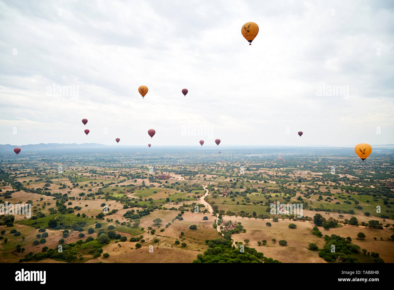 Hot air balloons fly over farmland with Buddhist temples in Bagan, Myanmar. Stock Photo
