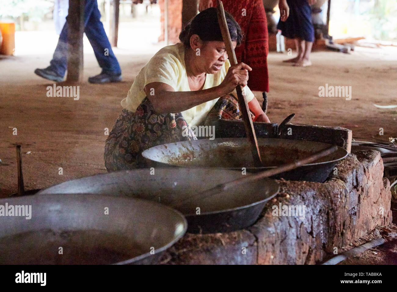 Woman stirs palmyra tree sap, boiled in pots to make sugar at market in Bagan, Myanmar Stock Photo