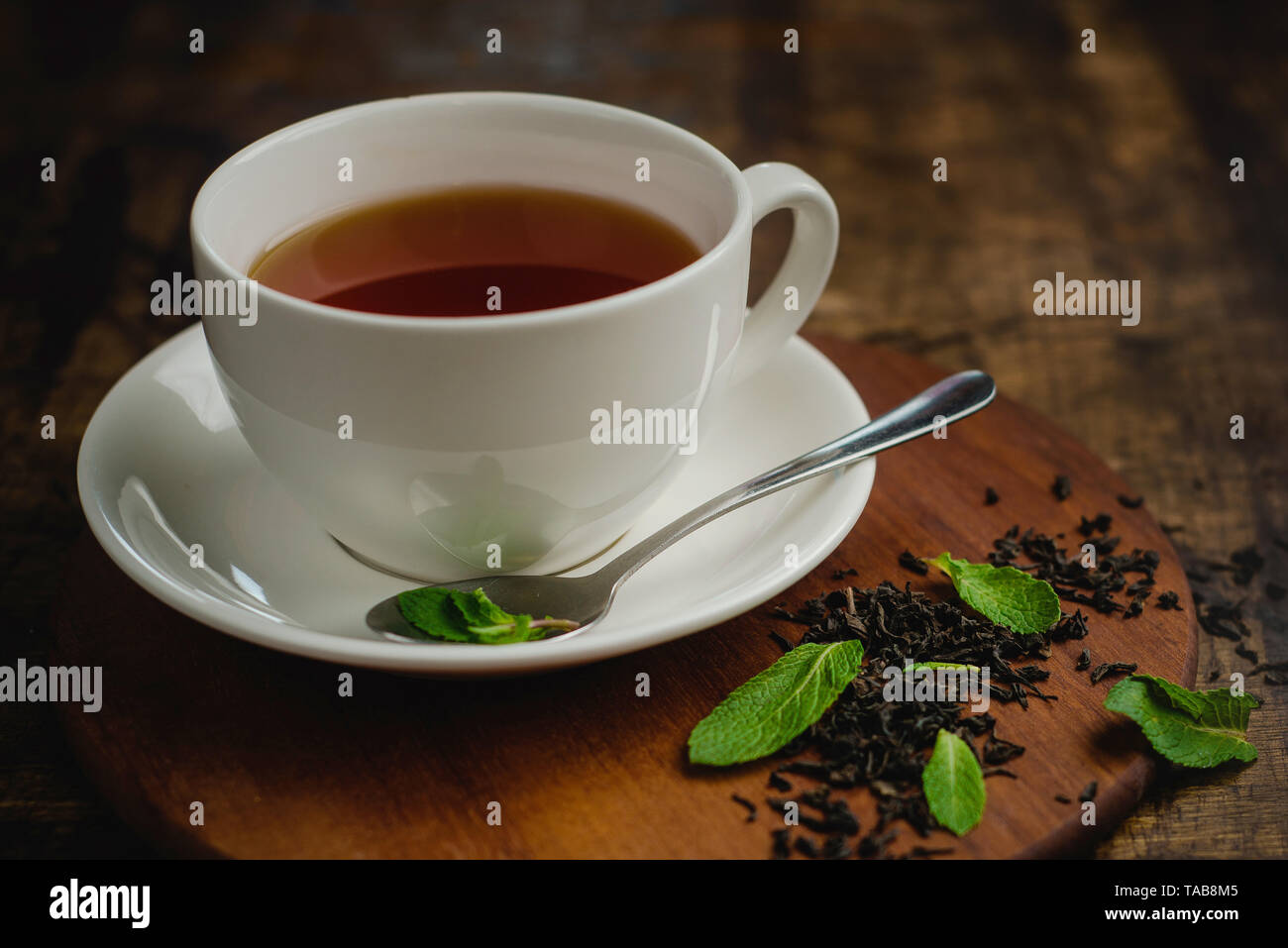 Mint tea in white porcelain cup on a warm wooden background with tea brew and mint leaves. Drink photo with copy space Stock Photo