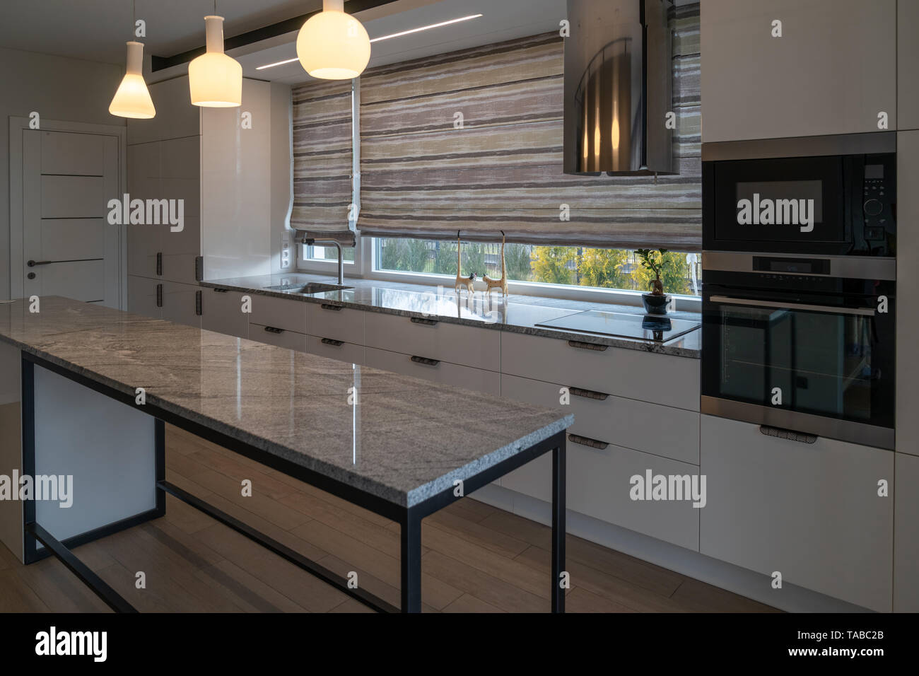 Modern kitchen furniture with marble worktops , drawers, cabinets, faucet by a kitchen sink, hob, steam collector, oven, electrical sockets. Stock Photo