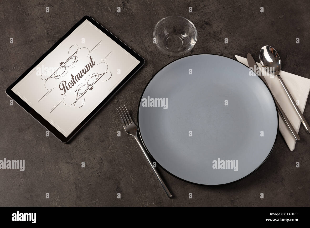 Tablet with stylish restaurant logo and laid table  Stock Photo