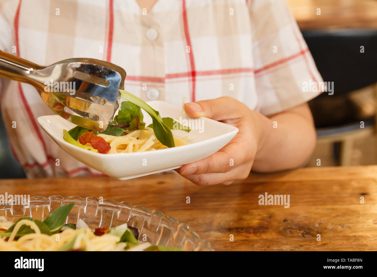 woman putting noodles into the dish on her hand Stock Photo