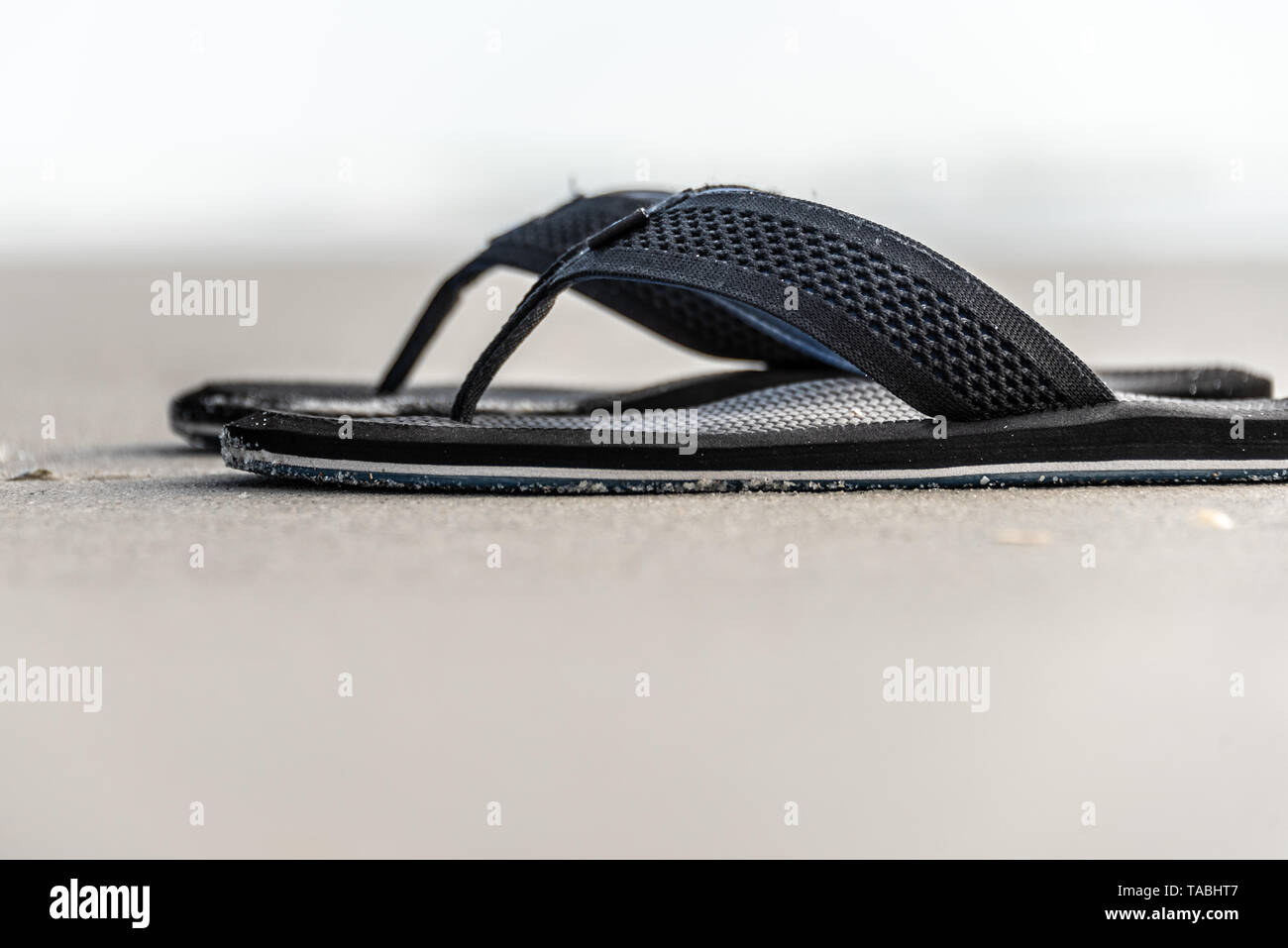Selective-focus, low-angle view of black sandals on wet beach sand. Stock Photo
