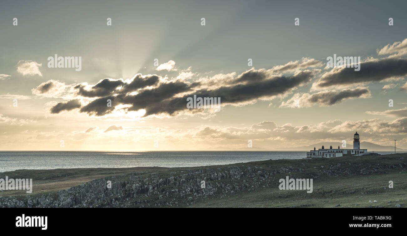 Seascape of Lighthouse on a rugged shoreline with clouds blocking the sun. Stock Photo