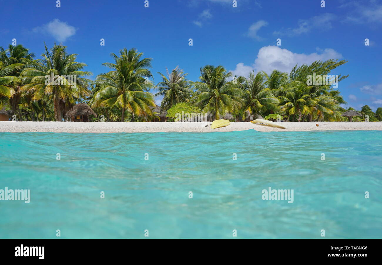 Tropical sea shore with kayaks on the beach and coconut trees with huts, seen from water surface, atoll of Tikehau, Tuamotu, French Polynesia, Pacific Stock Photo