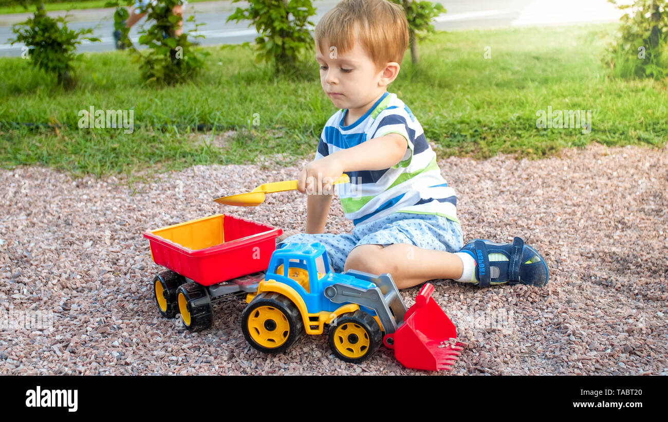 Closeup image of cute little boy playing on the palyground with toys. Child having fun with truck excavator and trailer. He is pretending to be a Stock Photo Alamy