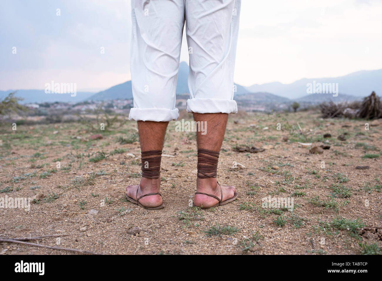 Man from behind standing on dry ground wearing white pants / trousers and ancient, gladiator style lace up sandals. RF outdoor concept. Oaxaca, Mexico Stock Photo