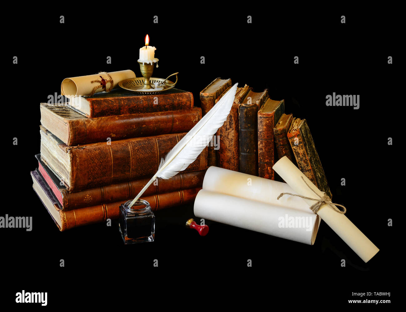 Many old books, rolls of manuscripts, white goose quill, inkwell and a burning candle in a copper candlestick isolated on a black background Stock Photo