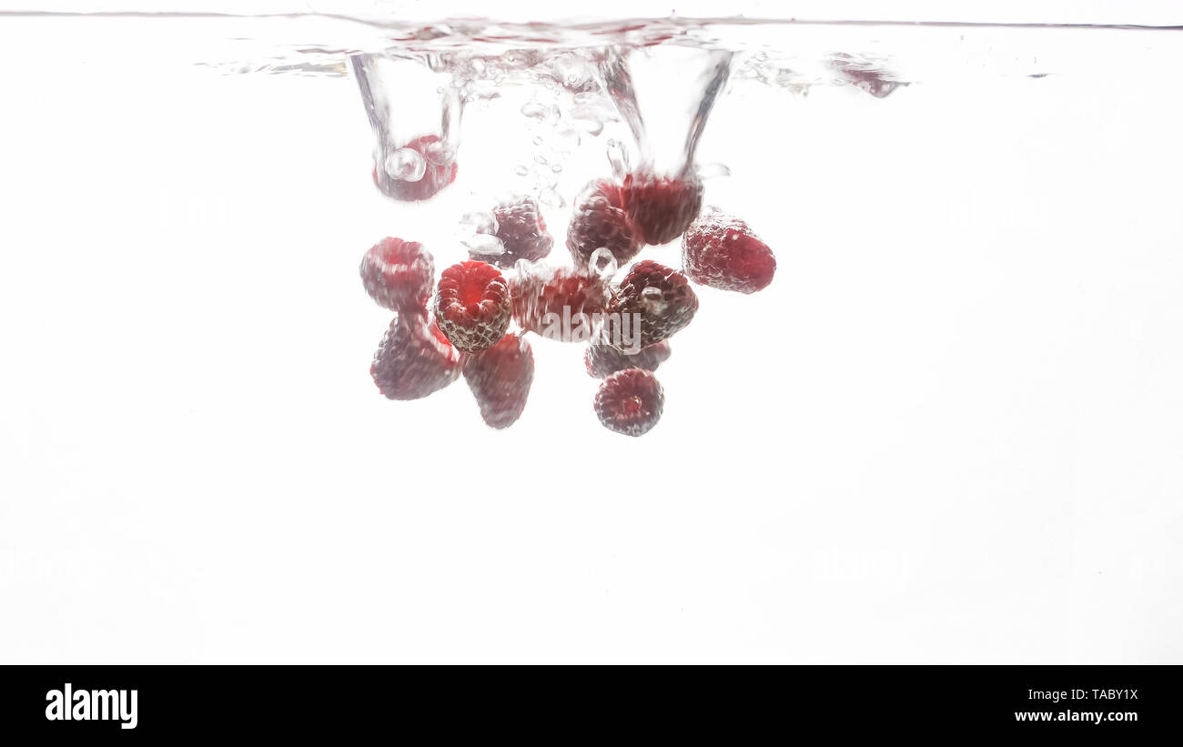 Closeup image of lots of fresh ripe raspberries falling and splashing ...