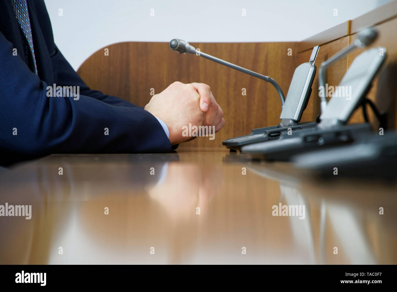 A businessman or a politician in a suit sits in front of a microphone while on duty, discussing or making a report. Without a face. Stock Photo
