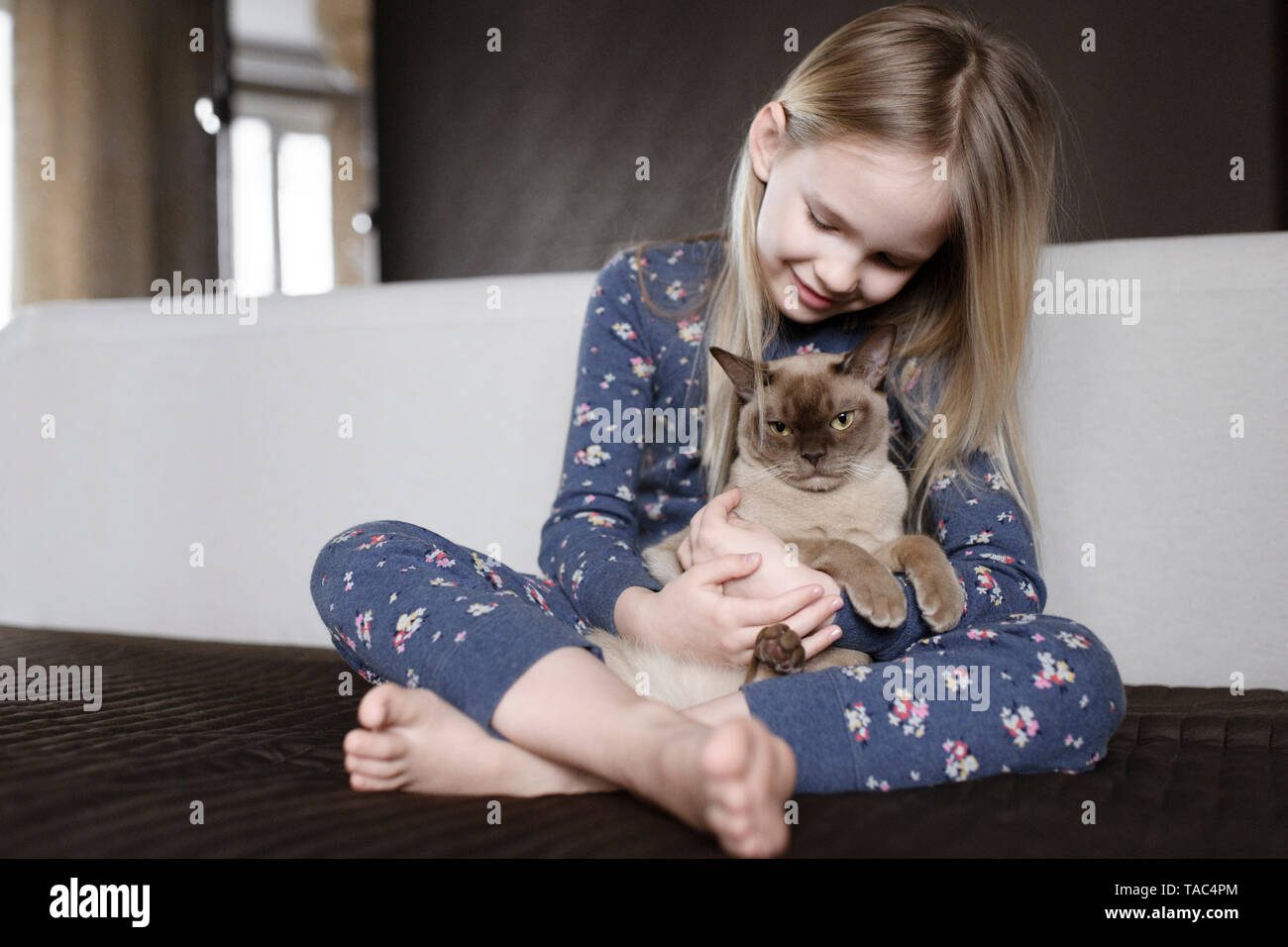 Smiling little girl wearing pyjama with floral design at home holding cat Stock Photo