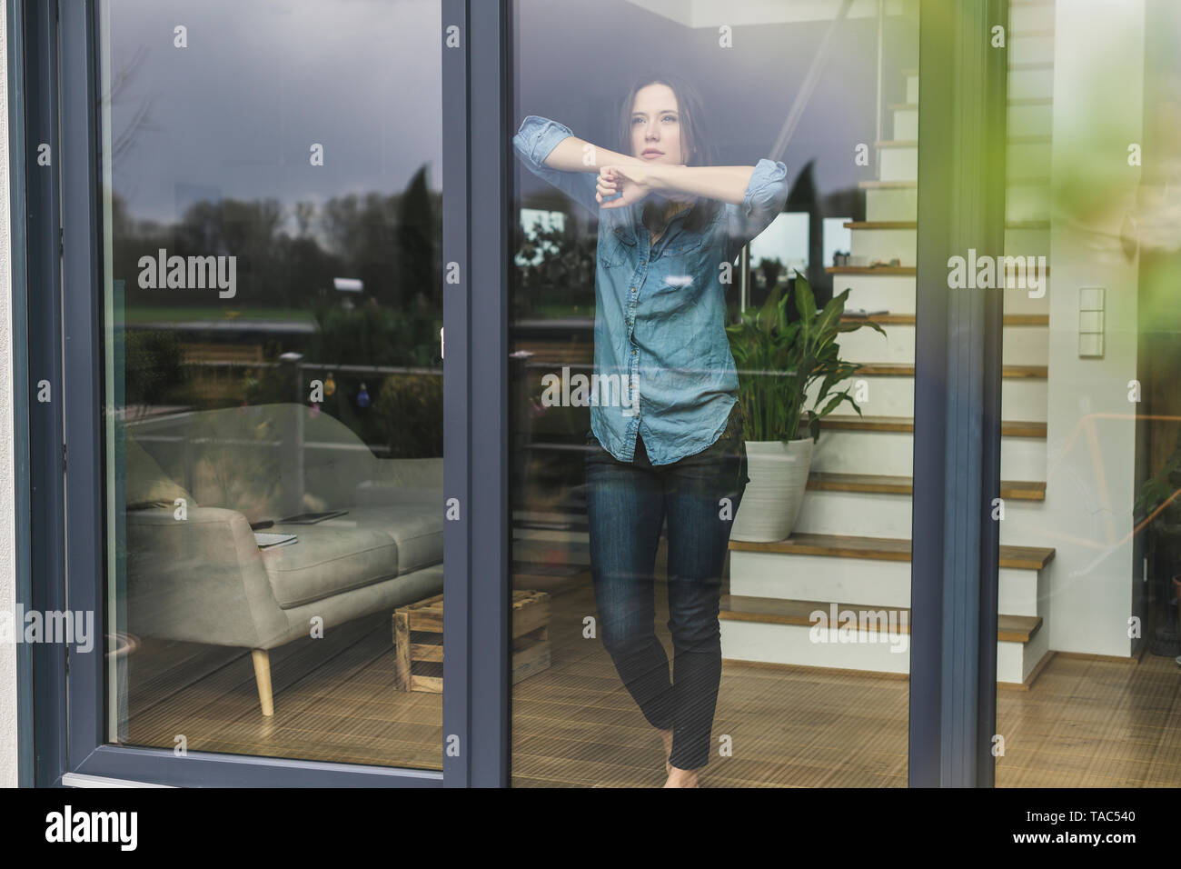 Serious woman standing behind terrace door at home Stock Photo