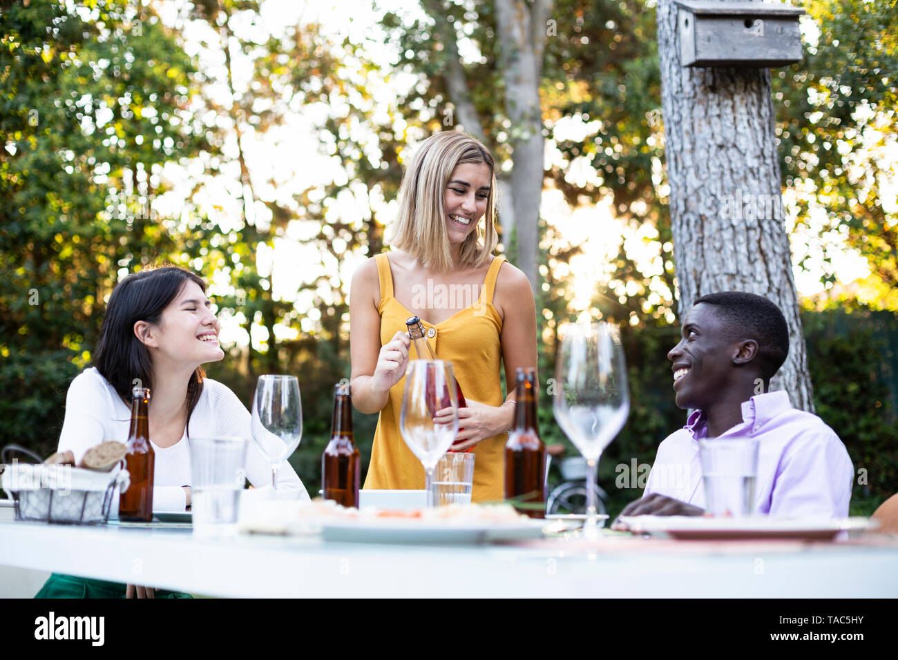 Friends at a summer dinner in the garden opening bottle of wine Stock Photo