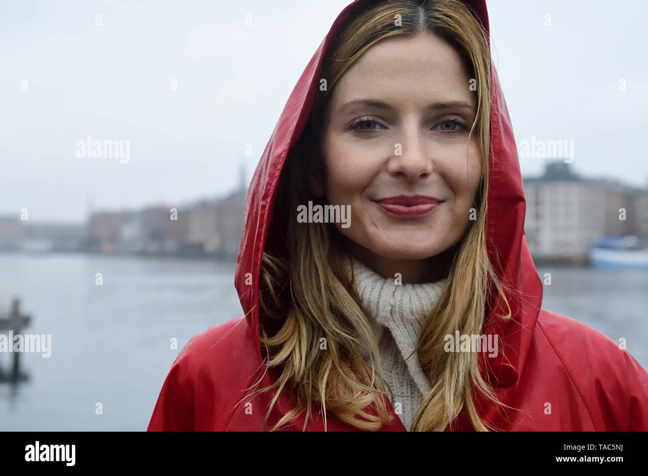 Denmark, Copenhagen, portrait of smiling woman at the waterfront in rainy weather Stock Photo