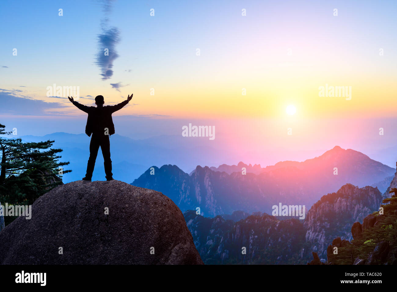 Hiker is standing on a rock with raised hands and enjoying sunrise Stock Photo