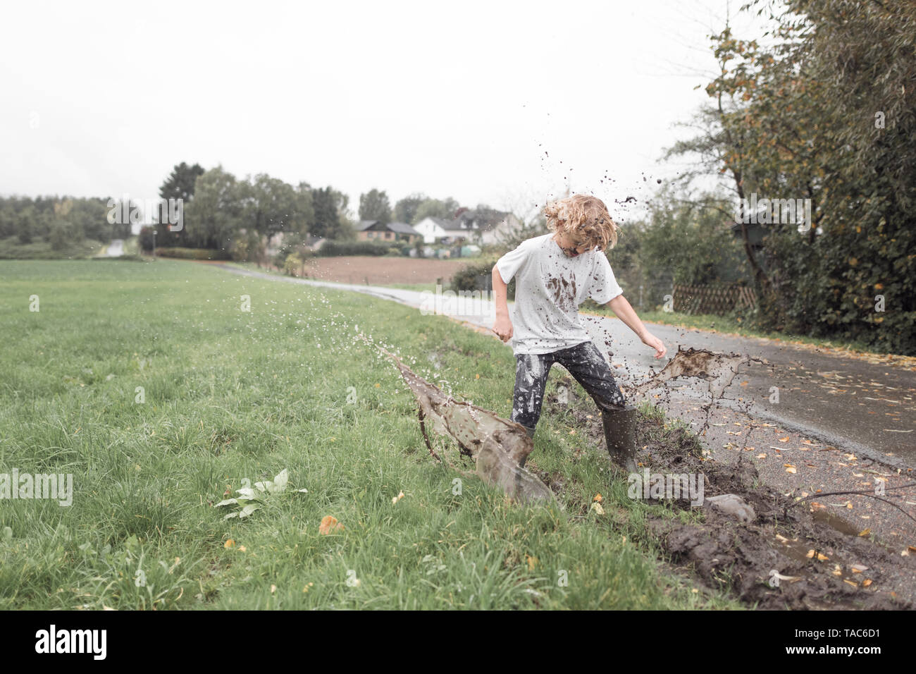 Boy jumping into a muddy puddle Stock Photo