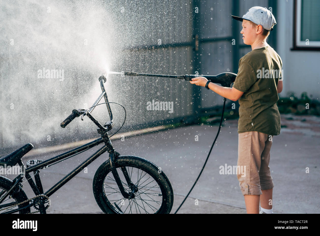Boy washing bmx bike with pressure washer on yard Stock Photo