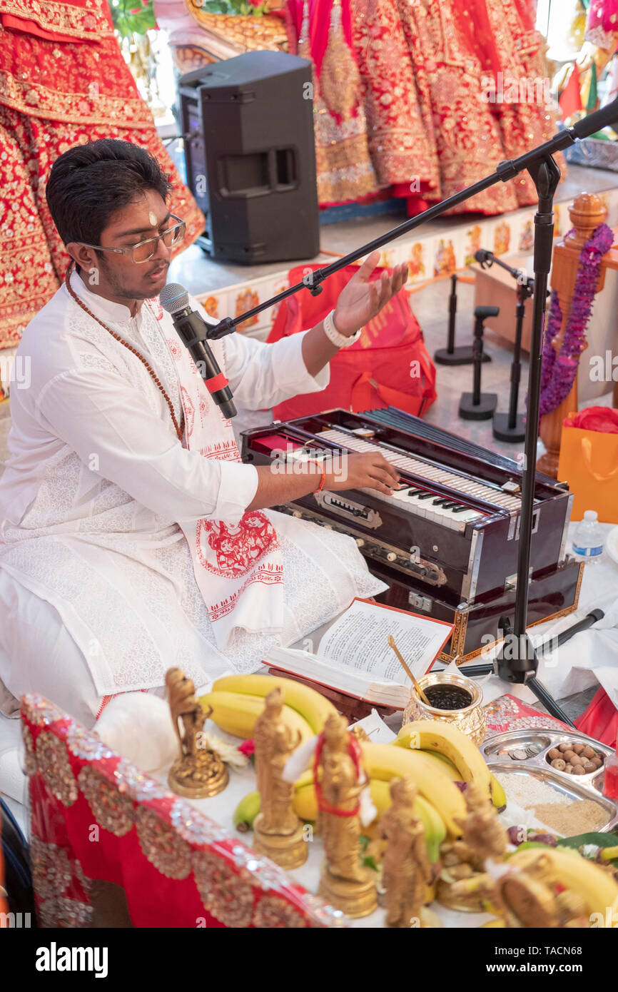A teenage prodigy priest singing a prayer and playing the harmonium at a Hindu temple in Jamaica, Queens, New York City, Stock Photo