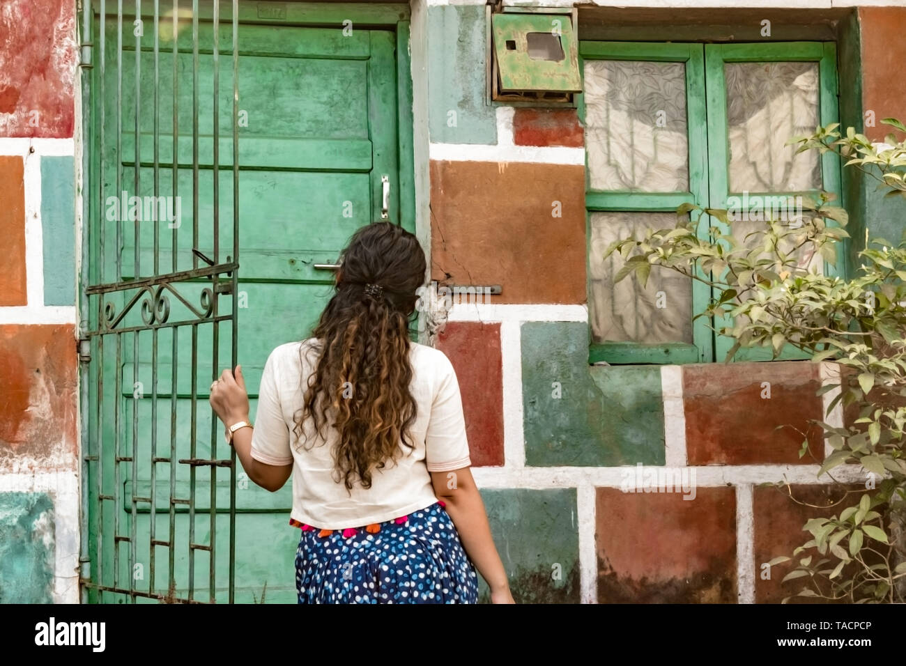 Back view of Girl with curly hair, opening the gate of colorful painted  house, wearing ethnic Indian wear, a white crop top and blue patiala  salwaar Stock Photo - Alamy