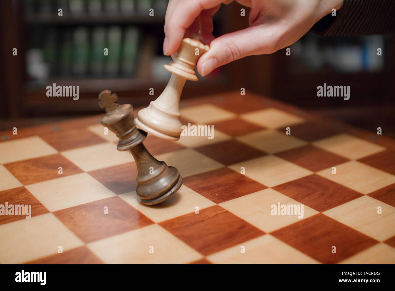 Concept: the woman who dominates the man. A woman's hand gives checkmate to  the king with the queen on a wooden chessboard, with no other pieces in  play Stock Photo