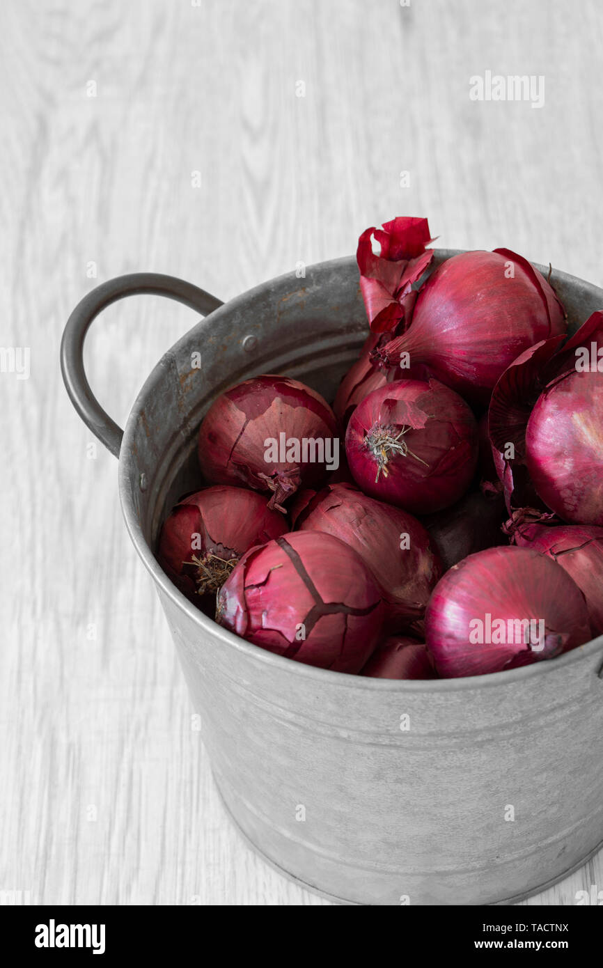 Red onions in a metal pot container with handle. Grey wood background