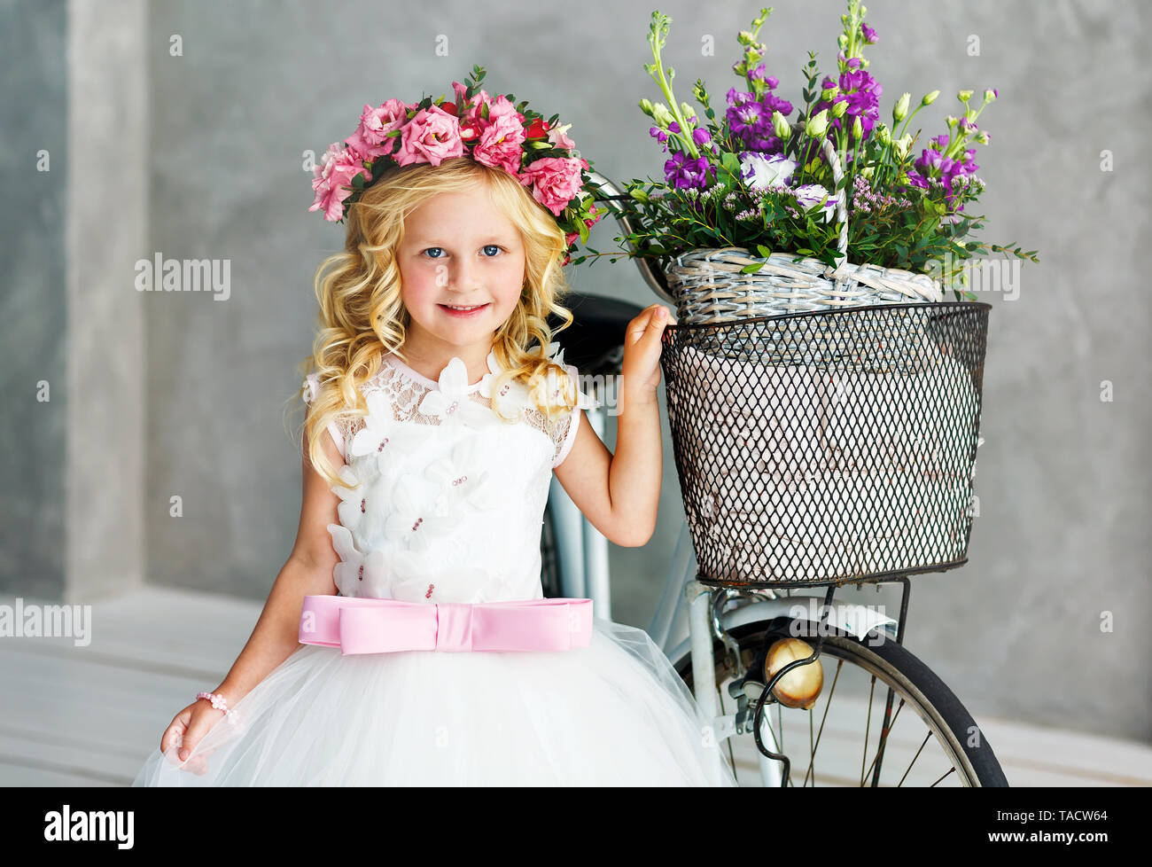 A cute little girl in a beautiful lush white dress in a wreath of ...