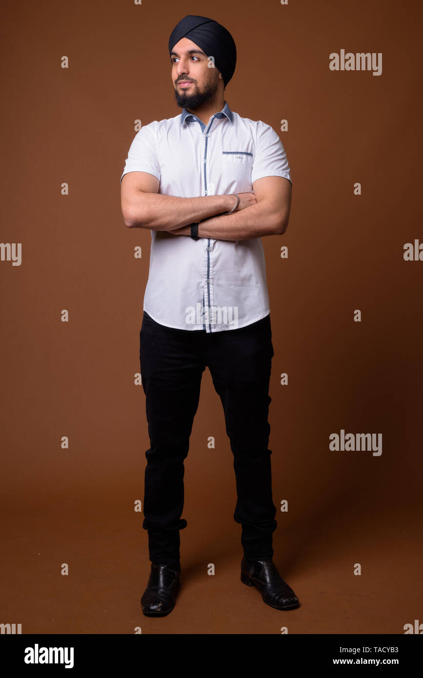 Studio shot of young bearded Indian Sikh man wearing smart casual clothes  against brown background Stock Photo