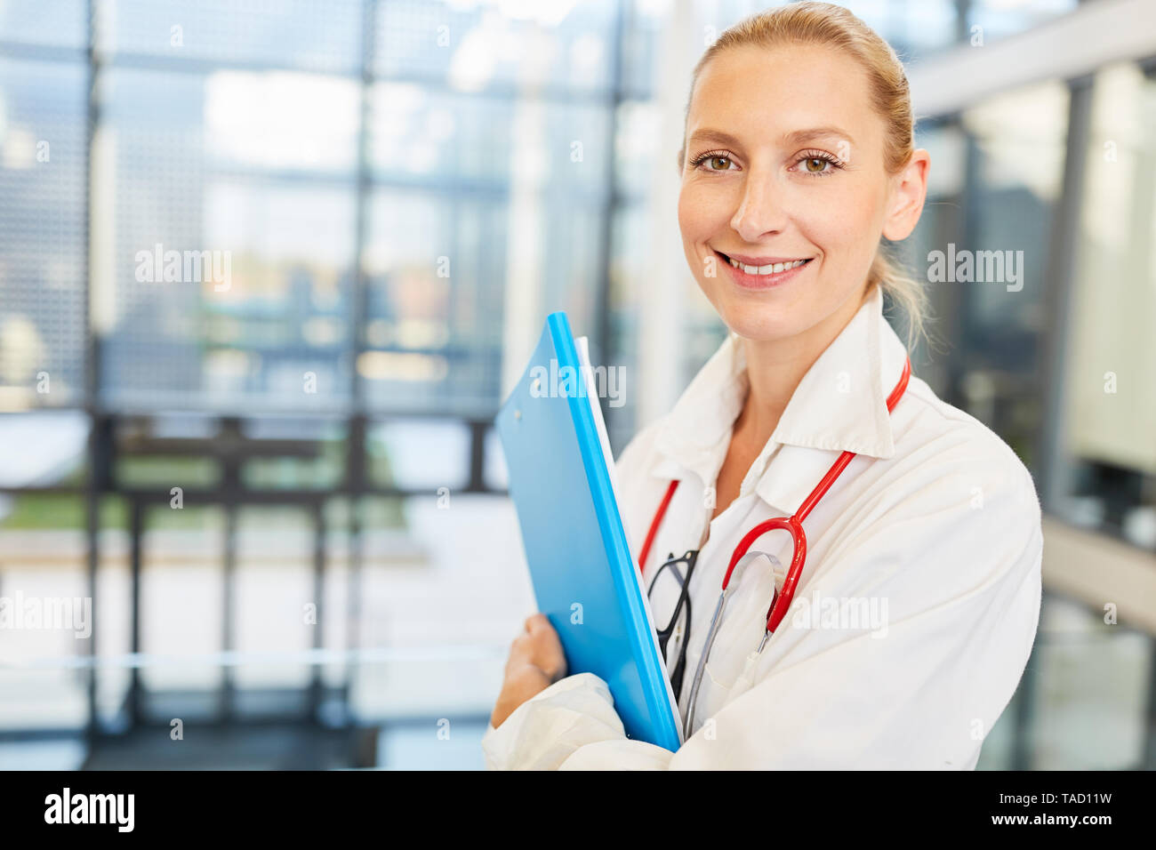 Young friendly female doctor in training or as a medical assistant with patient file Stock Photo