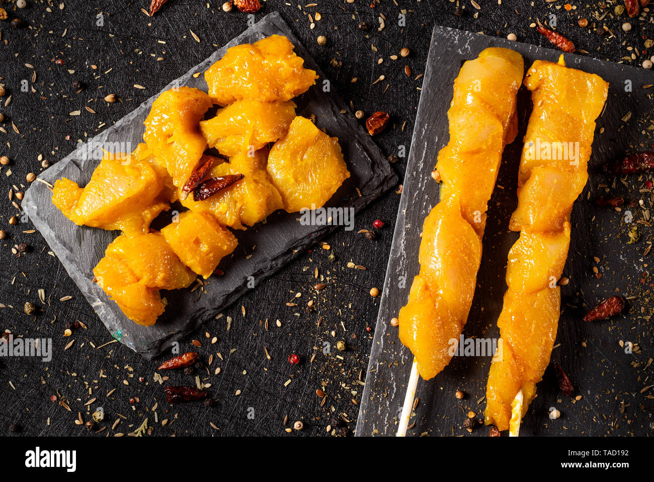 high angle view of some spiced raw chicken meat skewers and some dices of spiced raw chicken meat on two black slate plates, on a textile black surfac Stock Photo