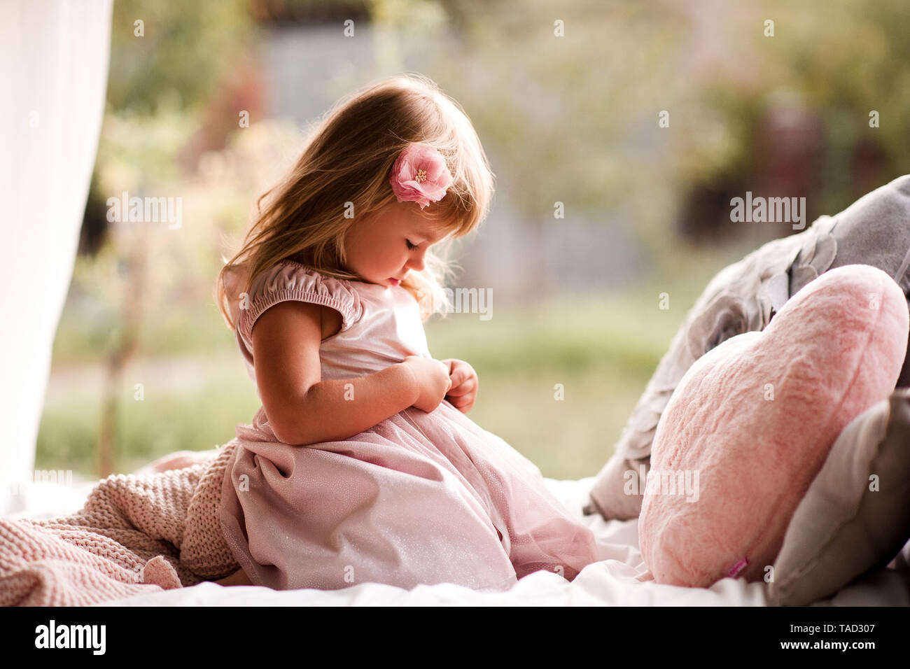 Cute baby girl 2-3 year old wearing stylish princess dress sitting in bed with pillows outdoors. Stock Photo