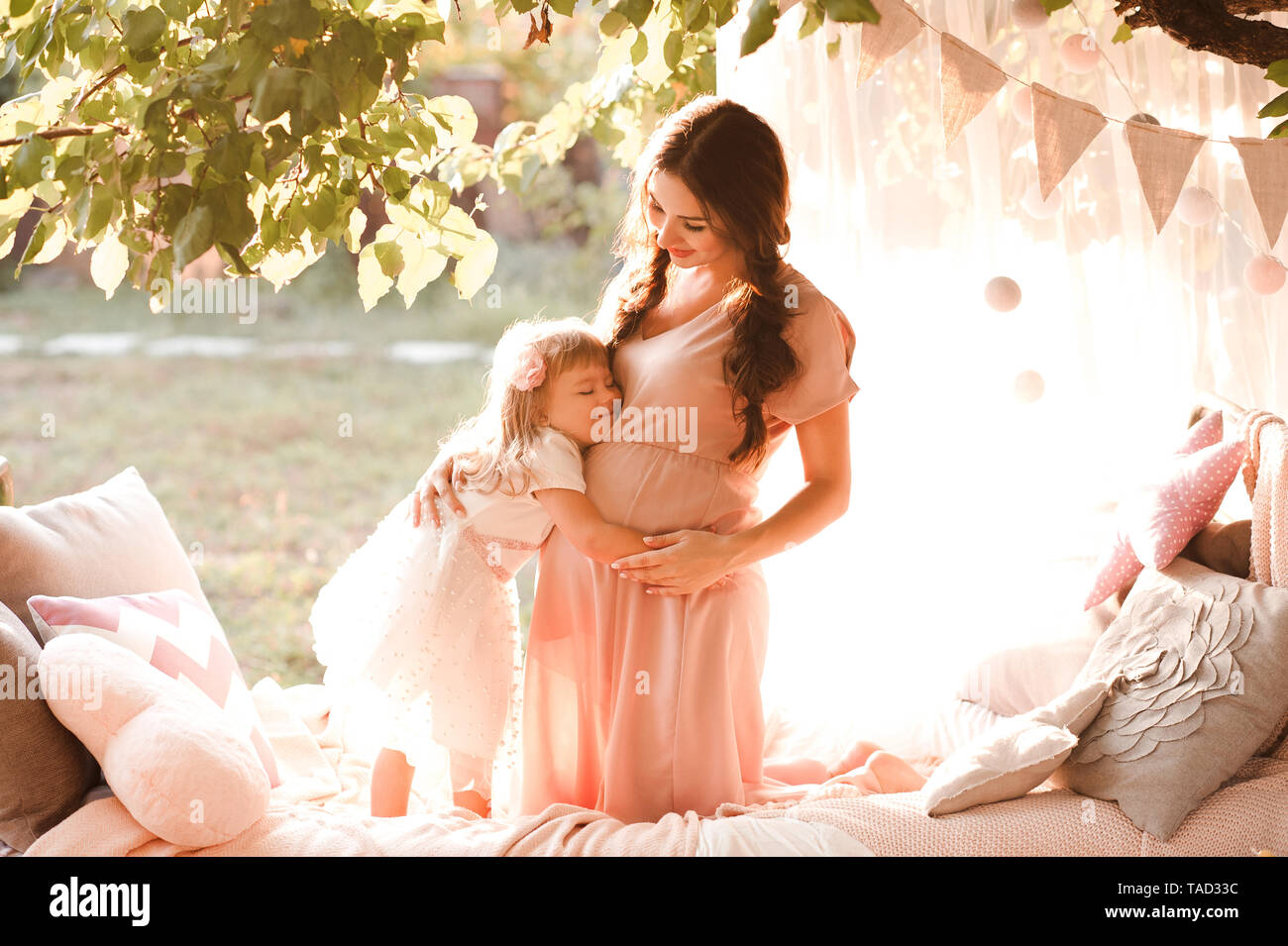 Pregnant mother holding kid girl 12 year old in bed outdoors