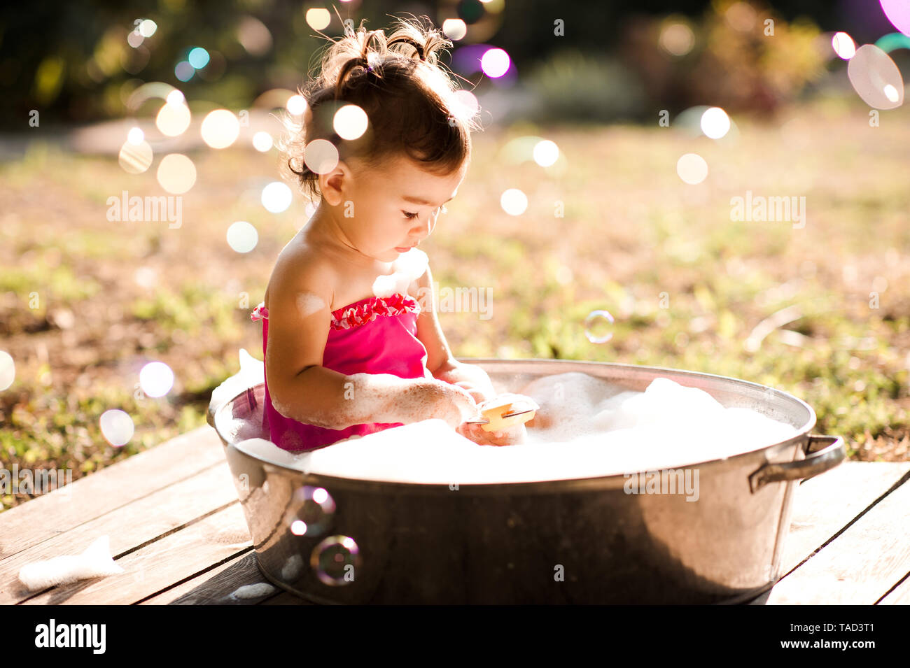 Funny baby girl 2-3 year old bathing outdoors with soap bubbles closeup