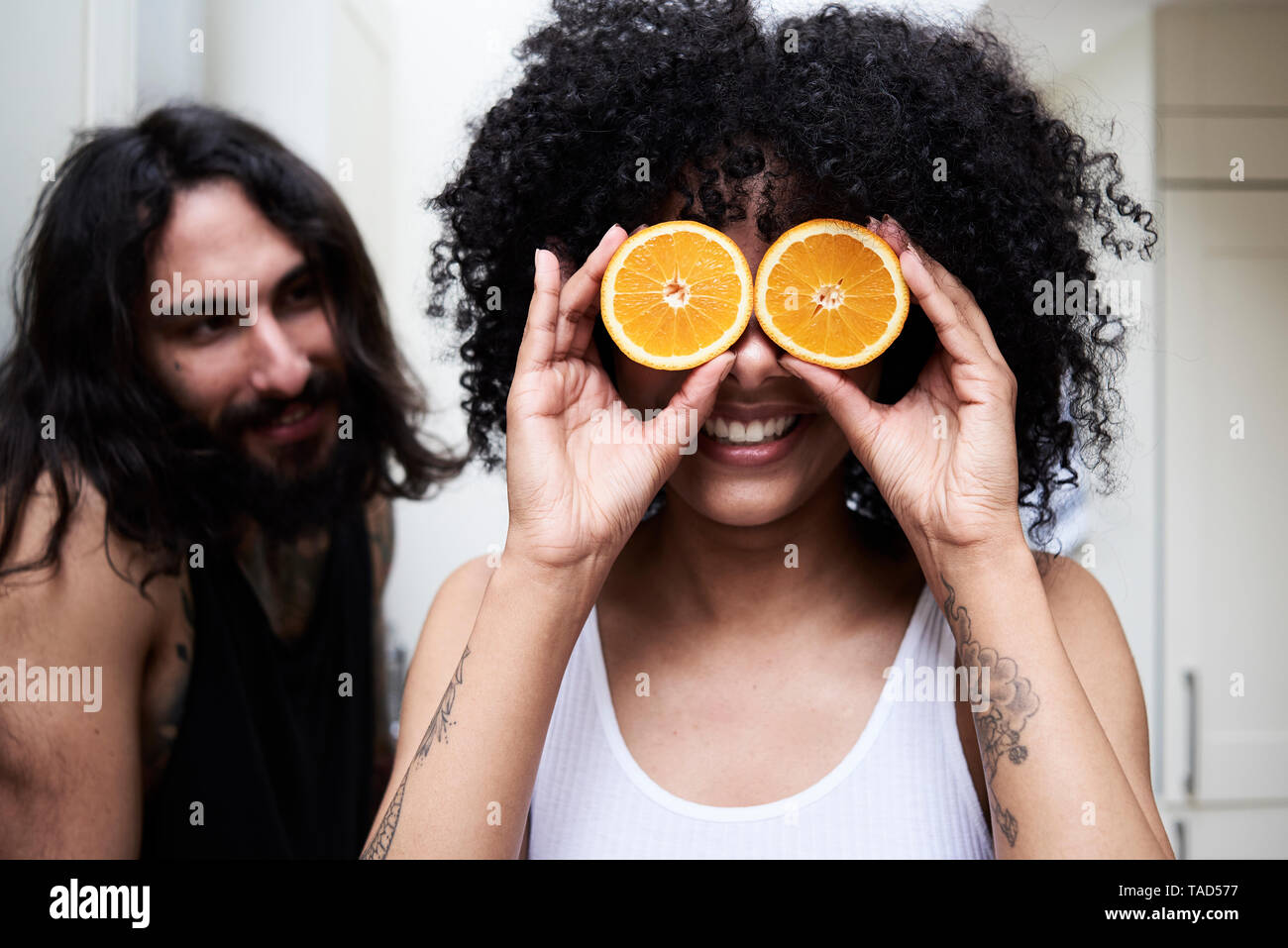 Happy young woman covering her eyes with oranges in kitchen Stock Photo