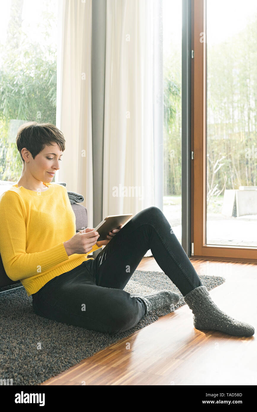 Woman sitting on the floor of living room using digital tablet Stock Photo