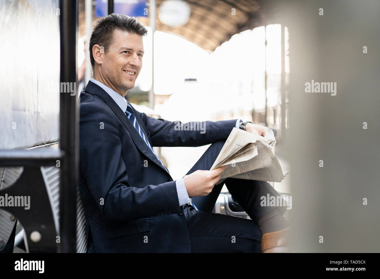 Smiling businessman reading newspaper on station platform Stock Photo