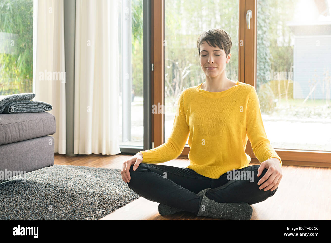 Portrait of woman sitting on the floor of living room meditating Stock Photo