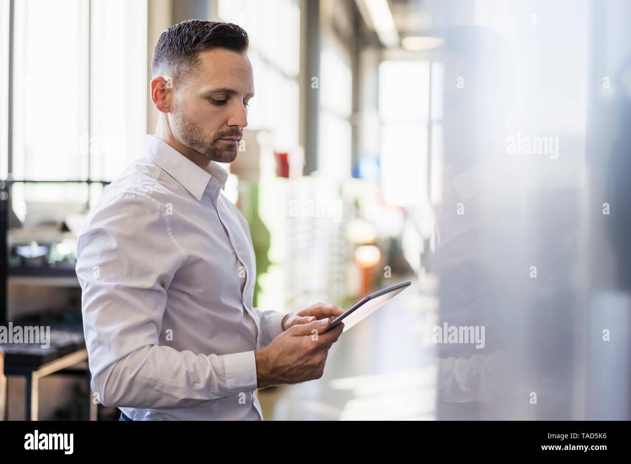 Businessman using tablet at a machine in modern factory Stock Photo