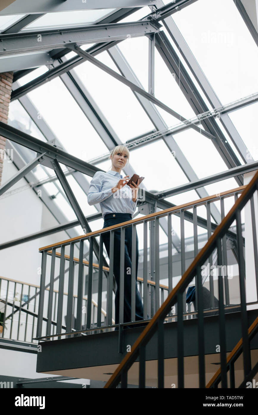 Businesswoman standing in loft office, using smartphone Stock Photo