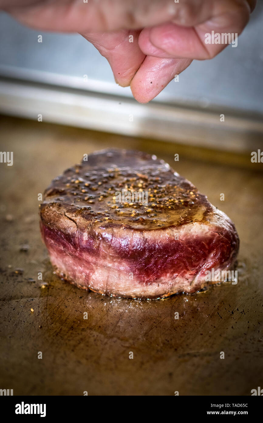 Female cook flavouring beef fillet with pepper Stock Photo