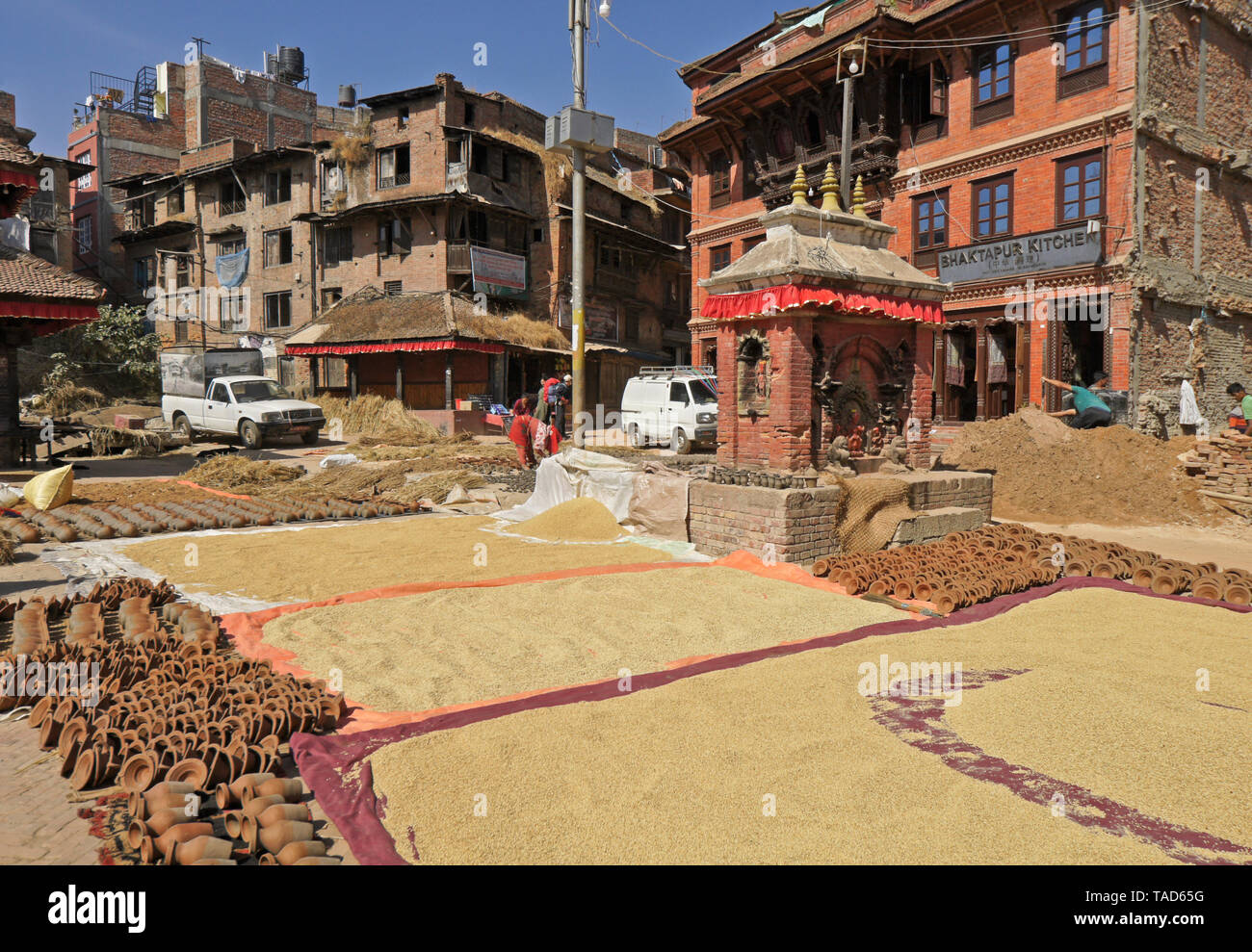 Clay pottery and harvested rice drying in sun next to Hindu shrine in Pottery Square, Bhaktapur, Kathmandu Valley, Nepal Stock Photo
