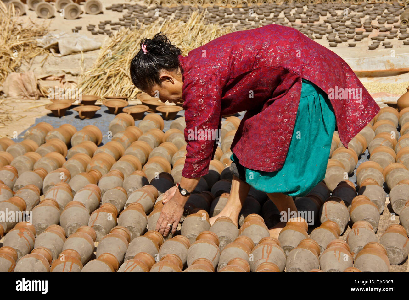 Woman turning clay pots as they sun-dry in Kumale Tol (Potters' Square, Pottery Square), Bhaktapur, Kathmandu Valley, Nepal Stock Photo