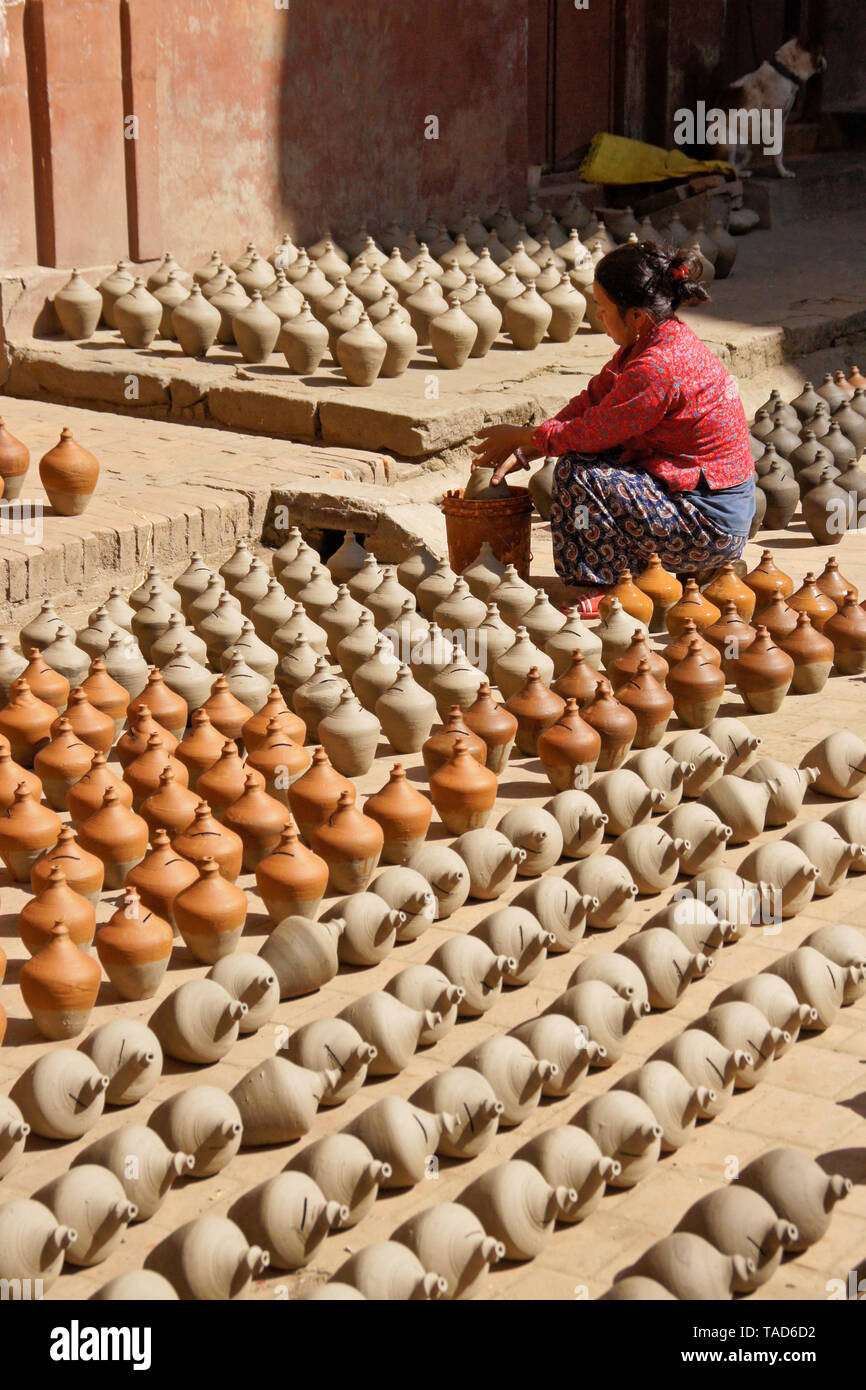 Woman dipping pottery into color as other clay products sun-dry near Kumale Tol (Potters' Square, Pottery Square),  Bhaktapur, Kathmandu Valley, Nepal Stock Photo