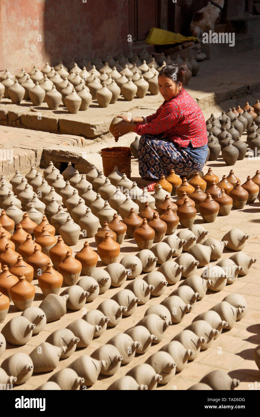 Woman dipping pottery into color as other clay products sun-dry near Kumale Tol (Potters' Square, Pottery Square),  Bhaktapur, Kathmandu Valley, Nepal Stock Photo