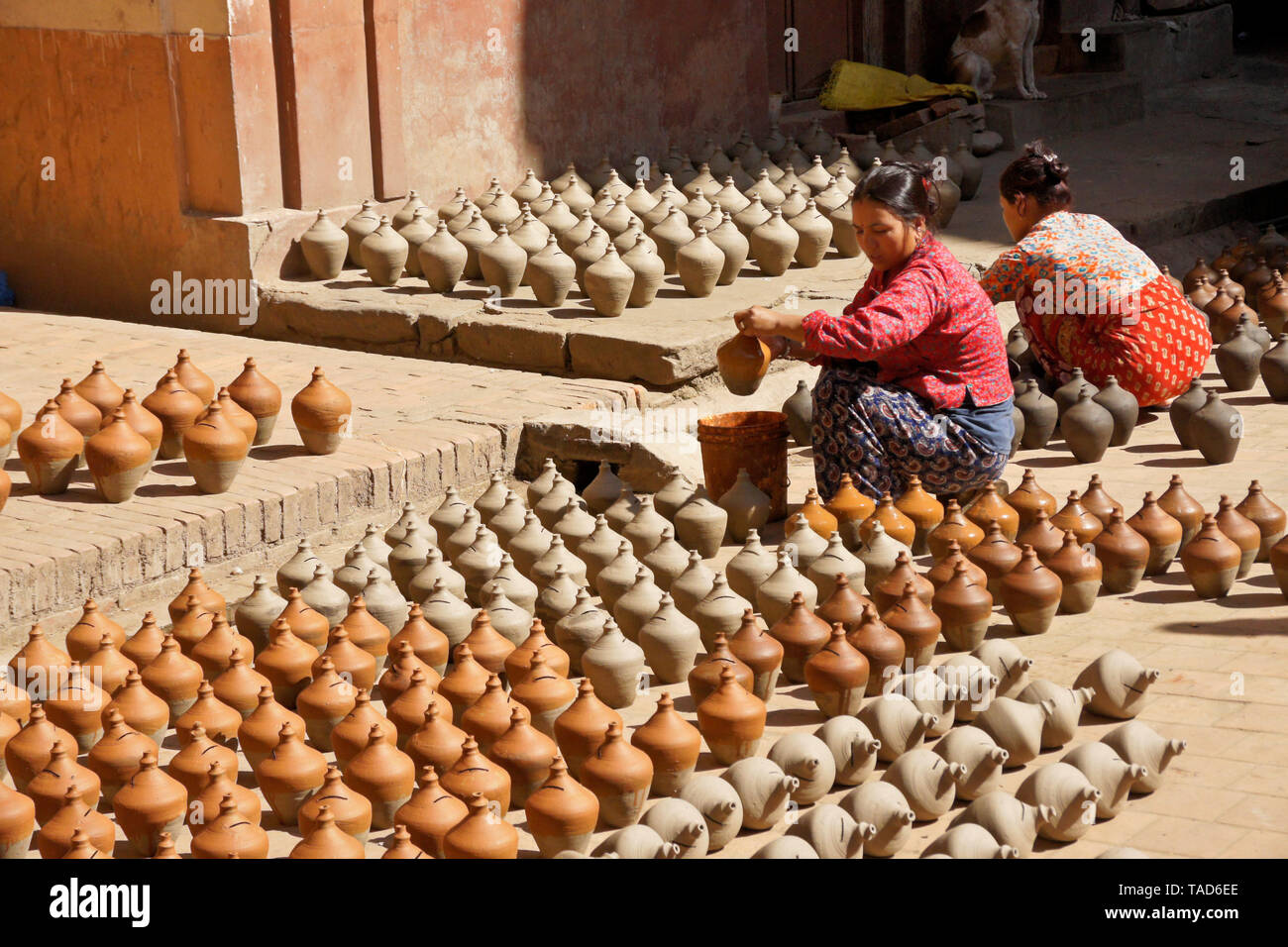 Women dipping pottery into color as other clay products sundry near