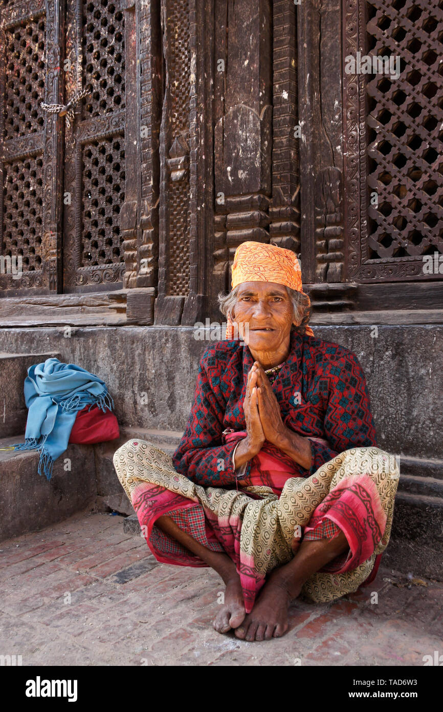 Elderly woman sitting with palms together in namaste greeting at Pashupati Mandir in Durbar Square, Bhaktapur, Kathmandu Valley, Nepal Stock Photo