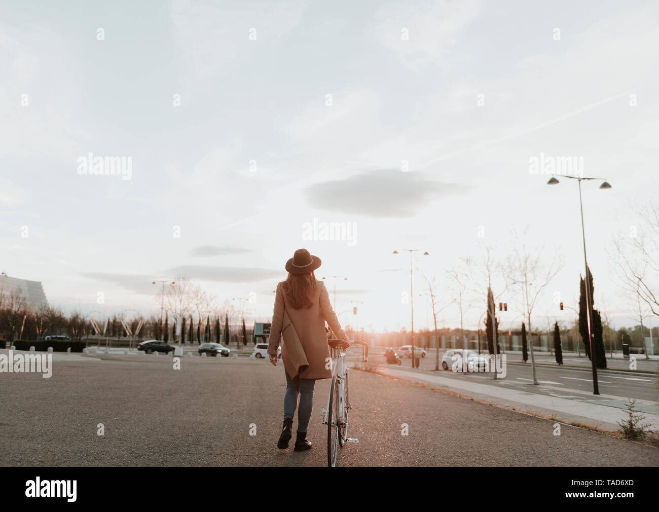 Young hipster woman going with a bicycle during sunset Stock Photo