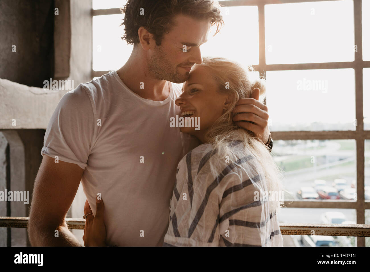 Happy young couple cuddling at the window Stock Photo - Alamy
